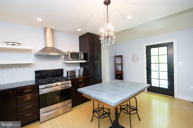 kitchen with stainless steel appliances, wall chimney range hood, a kitchen breakfast bar, backsplash, and a chandelier