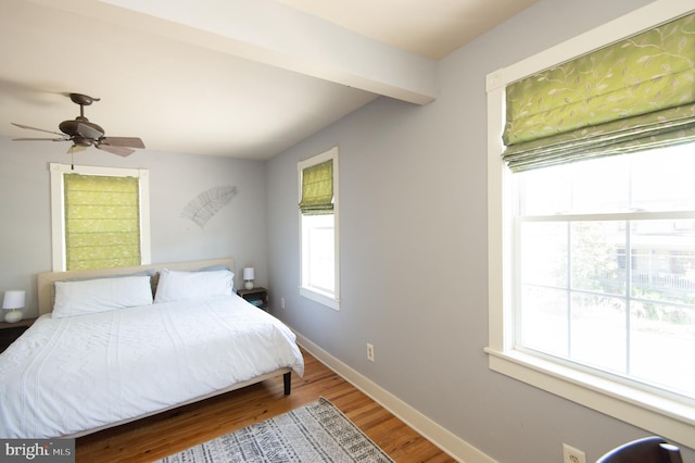 bedroom with beamed ceiling, ceiling fan, wood-type flooring, and multiple windows