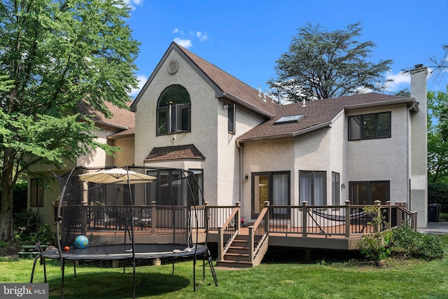 back of property featuring a lawn, a trampoline, and a deck