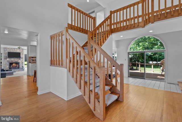 staircase with a fireplace, ceiling fan, hardwood / wood-style floors, and a towering ceiling