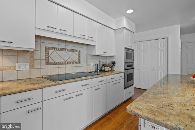 kitchen with white cabinets, wood-type flooring, backsplash, and stainless steel appliances