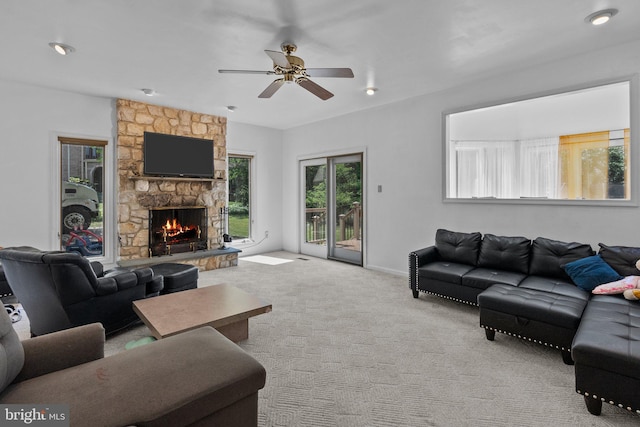 carpeted living room featuring ceiling fan and a stone fireplace