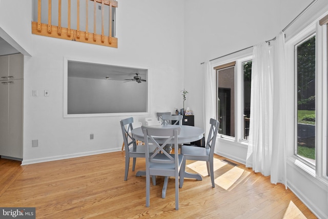 dining space featuring ceiling fan, light wood-type flooring, and a towering ceiling