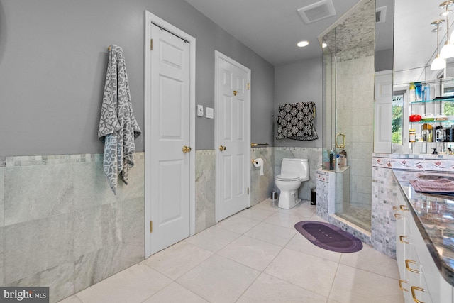 bathroom featuring tile patterned floors, toilet, tile walls, and walk in shower