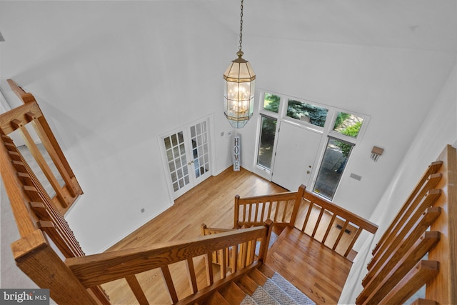 stairs with hardwood / wood-style floors, a notable chandelier, and high vaulted ceiling