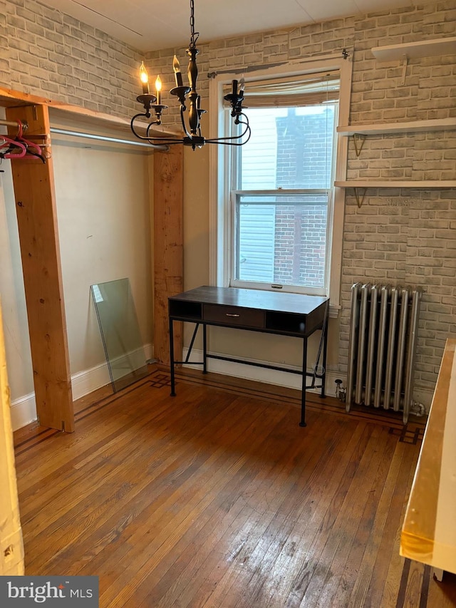 unfurnished dining area with hardwood / wood-style flooring, brick wall, radiator, and an inviting chandelier