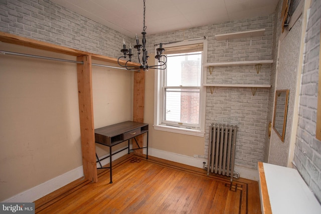 interior space with radiator, brick wall, baseboard heating, a notable chandelier, and light hardwood / wood-style floors