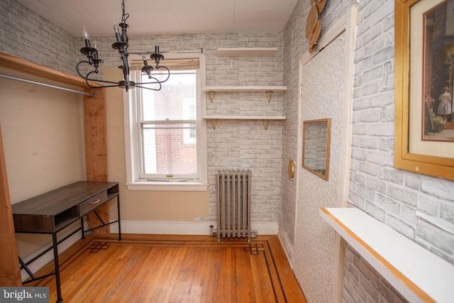 interior space featuring brick wall, light hardwood / wood-style flooring, radiator, and a chandelier