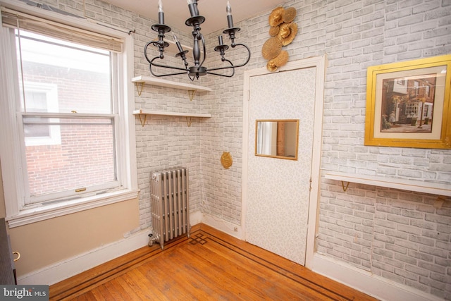 unfurnished dining area with radiator, light hardwood / wood-style flooring, brick wall, and an inviting chandelier