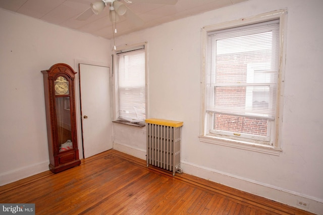 empty room with hardwood / wood-style floors, ceiling fan, radiator heating unit, and a wealth of natural light