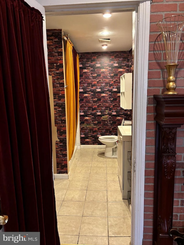 bathroom featuring vanity, tile patterned flooring, toilet, washer / dryer, and brick wall