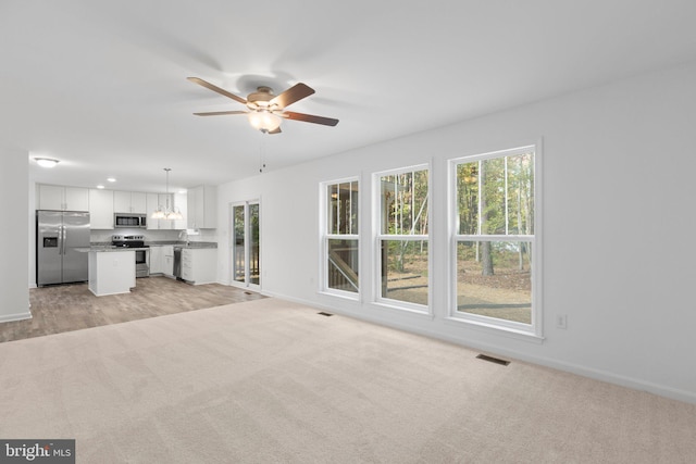 unfurnished living room featuring ceiling fan and light colored carpet