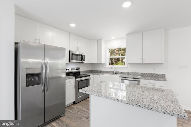 kitchen with white cabinetry, a center island, stainless steel appliances, and light hardwood / wood-style flooring