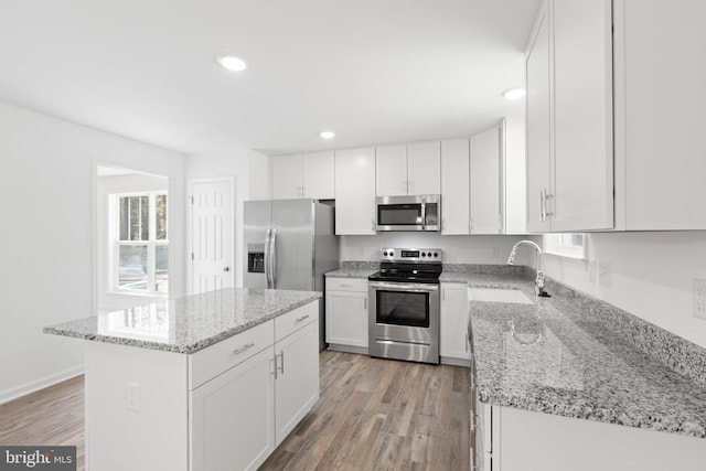 kitchen with appliances with stainless steel finishes, light stone counters, a kitchen island, light hardwood / wood-style floors, and white cabinetry