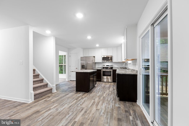 kitchen featuring light stone countertops, white cabinetry, a center island, appliances with stainless steel finishes, and light wood-type flooring