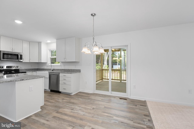 kitchen featuring light wood-type flooring, a wealth of natural light, stainless steel appliances, decorative light fixtures, and white cabinets