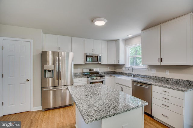 kitchen with stainless steel appliances, sink, white cabinetry, light hardwood / wood-style floors, and a kitchen island