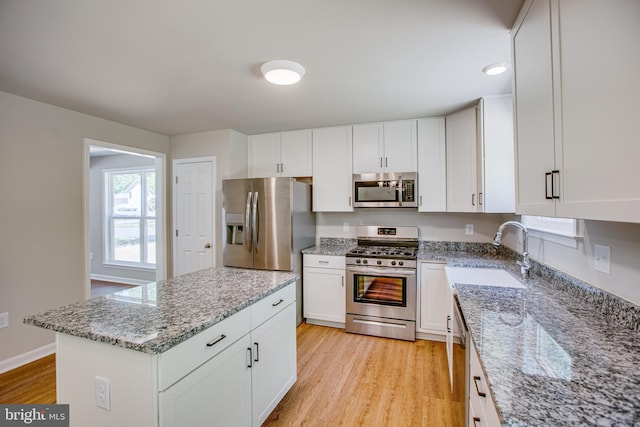 kitchen with stainless steel appliances, light stone counters, light hardwood / wood-style floors, and sink