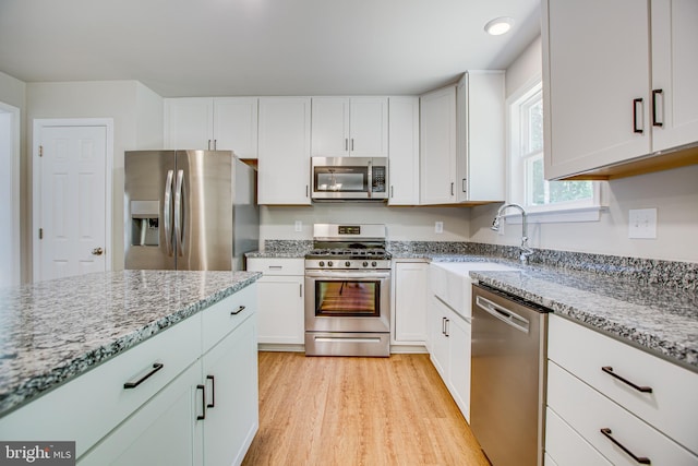 kitchen featuring light stone countertops, light wood-type flooring, stainless steel appliances, sink, and white cabinetry