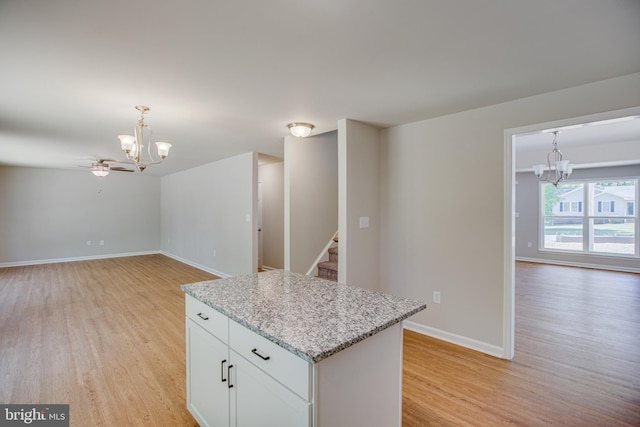 kitchen featuring light stone counters, light hardwood / wood-style flooring, white cabinets, a kitchen island, and hanging light fixtures