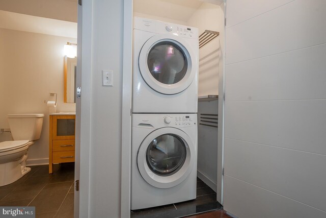 laundry room featuring dark tile patterned flooring and stacked washing maching and dryer