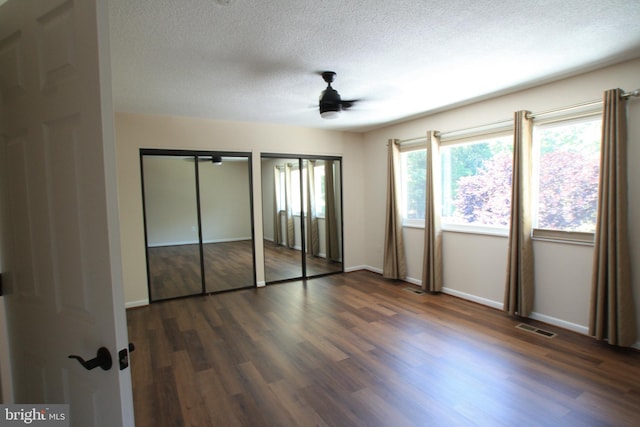 unfurnished bedroom with a textured ceiling, dark hardwood / wood-style flooring, ceiling fan, and multiple closets