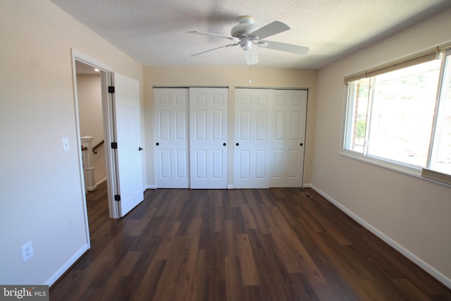 unfurnished bedroom with multiple closets, ceiling fan, dark wood-type flooring, and a textured ceiling