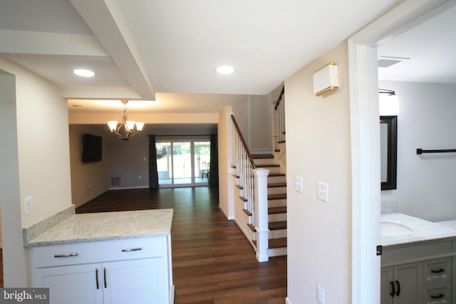 kitchen with white cabinetry, dark wood-type flooring, light stone counters, and an inviting chandelier