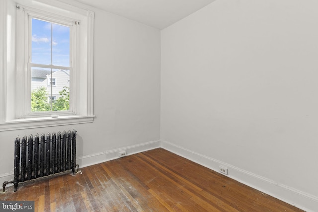 empty room with dark hardwood / wood-style flooring and radiator heating unit