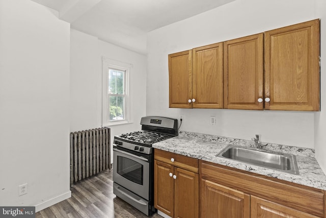 kitchen with sink, stainless steel gas range, dark hardwood / wood-style flooring, light stone counters, and radiator heating unit