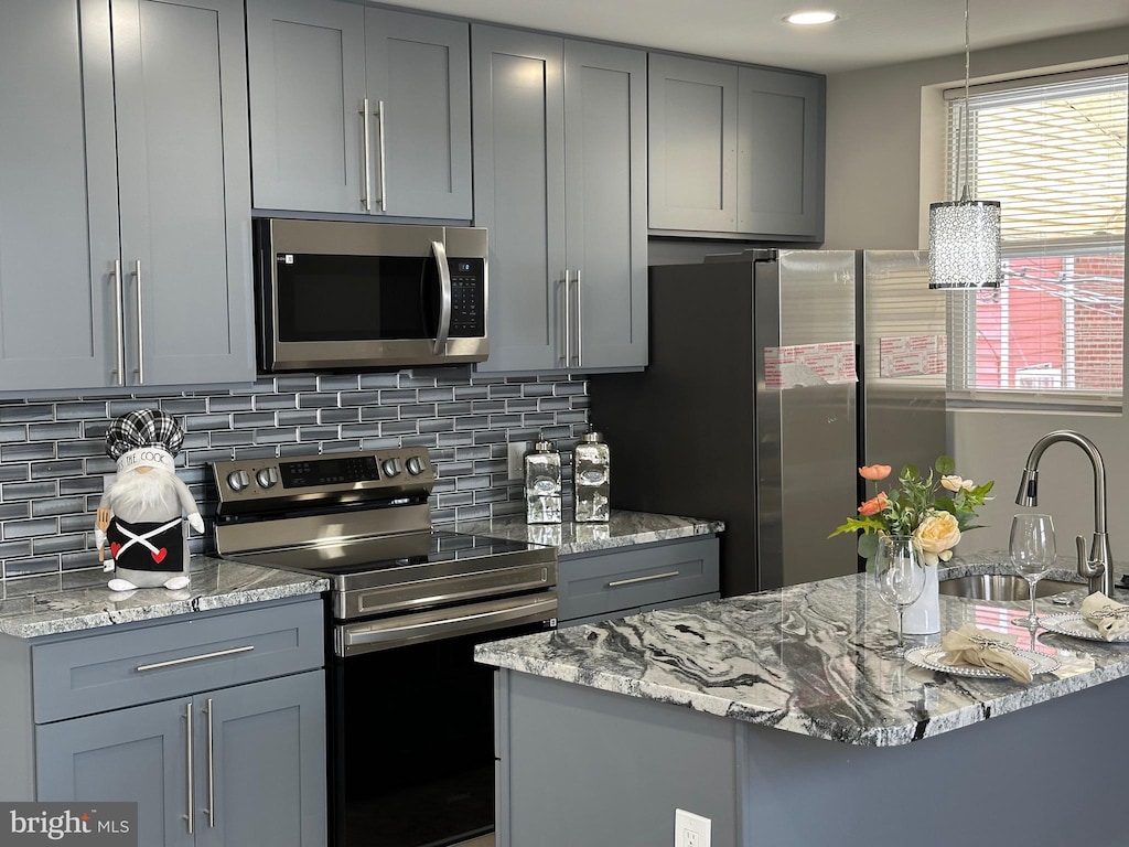 kitchen featuring decorative backsplash, light stone counters, gray cabinetry, stainless steel appliances, and sink