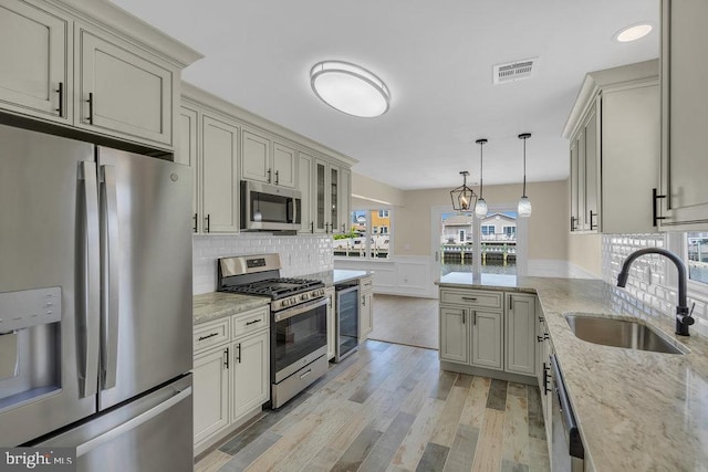 kitchen with sink, hanging light fixtures, light hardwood / wood-style floors, light stone counters, and stainless steel appliances