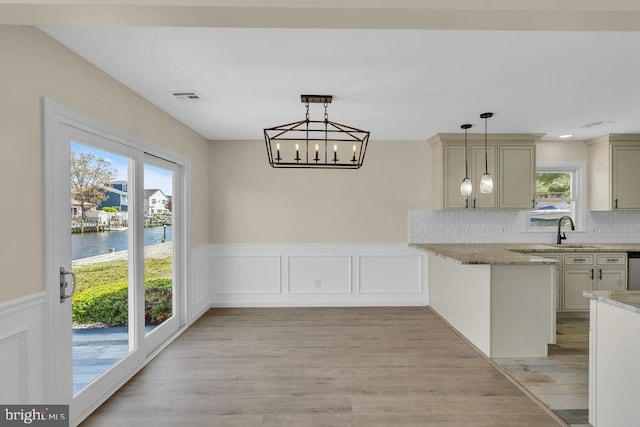 kitchen featuring kitchen peninsula, backsplash, pendant lighting, a water view, and light hardwood / wood-style flooring