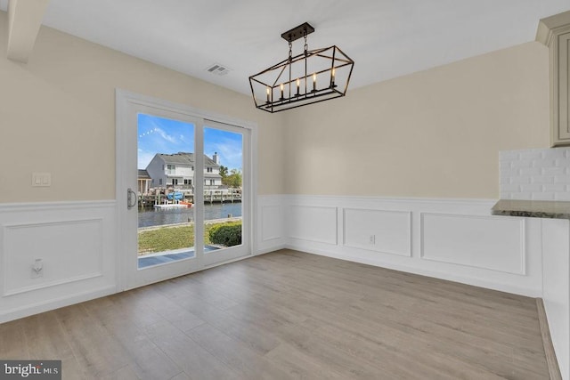 unfurnished dining area featuring a chandelier, a water view, and light hardwood / wood-style floors