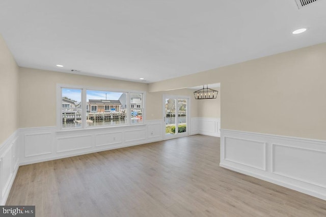 spare room featuring a water view, a healthy amount of sunlight, a notable chandelier, and light hardwood / wood-style floors