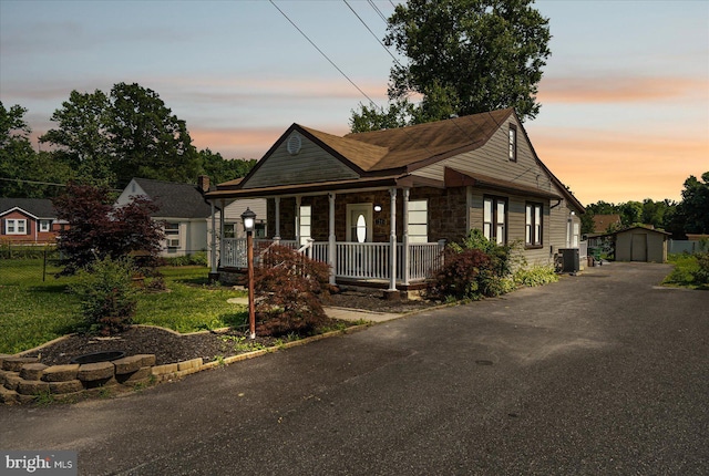 view of front of house with a lawn, a porch, an outdoor structure, and central AC