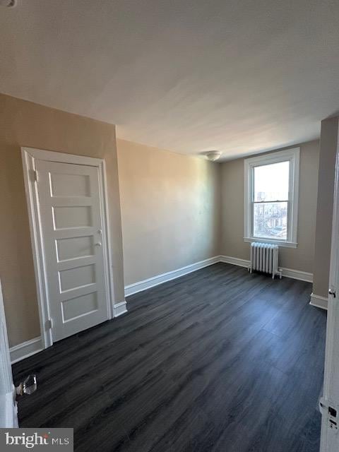 unfurnished room with radiator heating unit and dark hardwood / wood-style floors