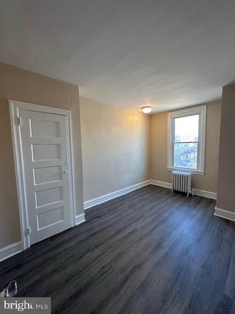 spare room with dark wood-type flooring and radiator heating unit