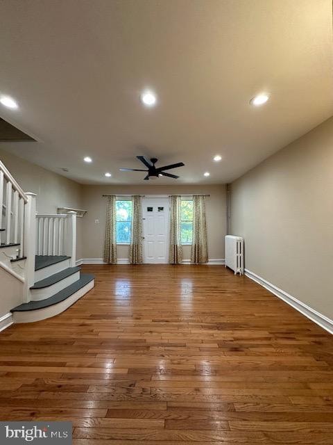 unfurnished living room with wood-type flooring, radiator, and ceiling fan