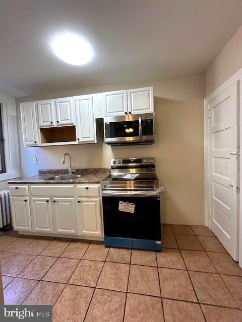 kitchen with appliances with stainless steel finishes, light tile patterned flooring, sink, radiator heating unit, and white cabinetry