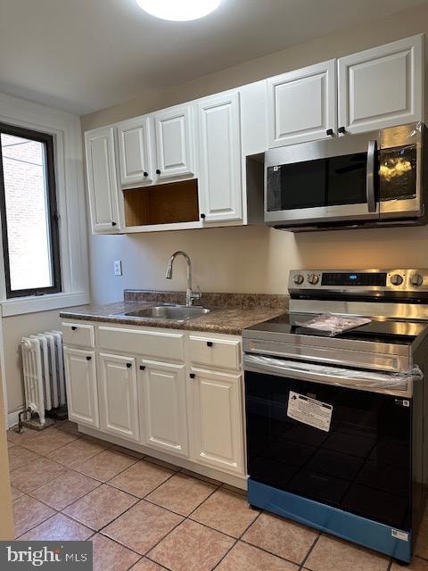 kitchen with appliances with stainless steel finishes, white cabinetry, sink, and radiator