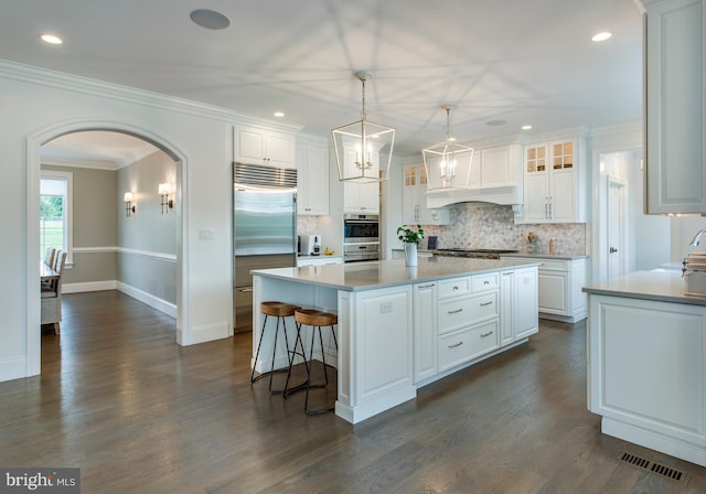 kitchen featuring a center island, dark wood-type flooring, stainless steel appliances, decorative light fixtures, and white cabinets