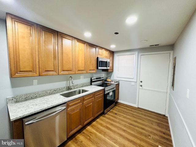 kitchen with light stone countertops, stainless steel appliances, light hardwood / wood-style flooring, and sink