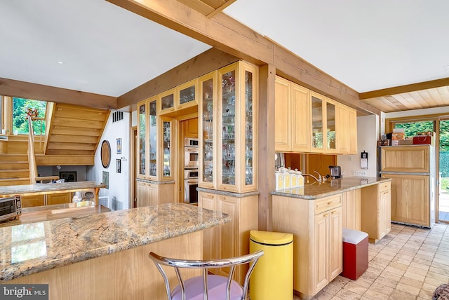 kitchen with light stone counters, lofted ceiling, kitchen peninsula, and light brown cabinetry