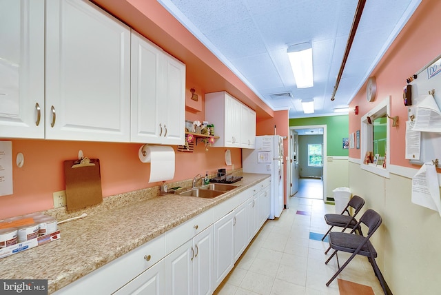 kitchen featuring light stone countertops, white fridge, white cabinetry, and sink