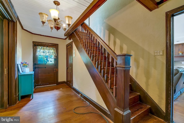 stairs with wood-type flooring, wooden ceiling, an inviting chandelier, and crown molding