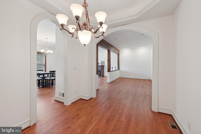 unfurnished dining area with wood-type flooring, a tray ceiling, an inviting chandelier, and ornamental molding