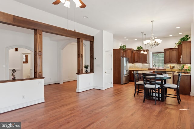 dining space featuring ceiling fan with notable chandelier, sink, and light hardwood / wood-style flooring