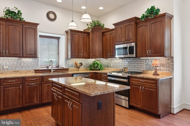 kitchen with pendant lighting, sink, light wood-type flooring, a kitchen island, and stainless steel appliances