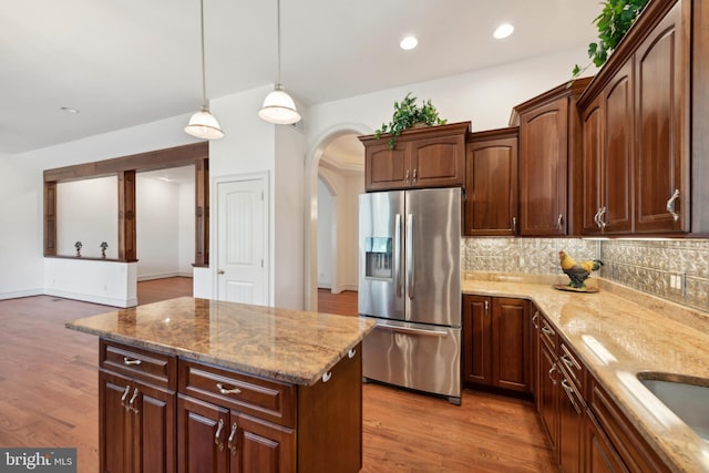 kitchen featuring stainless steel fridge, hanging light fixtures, light stone counters, and light wood-type flooring